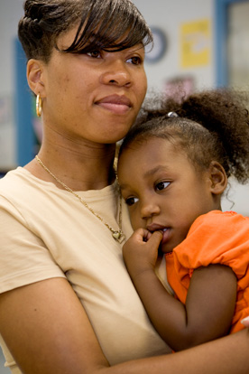 Woman holds young girl in her arms while the girl rests on her shoulder