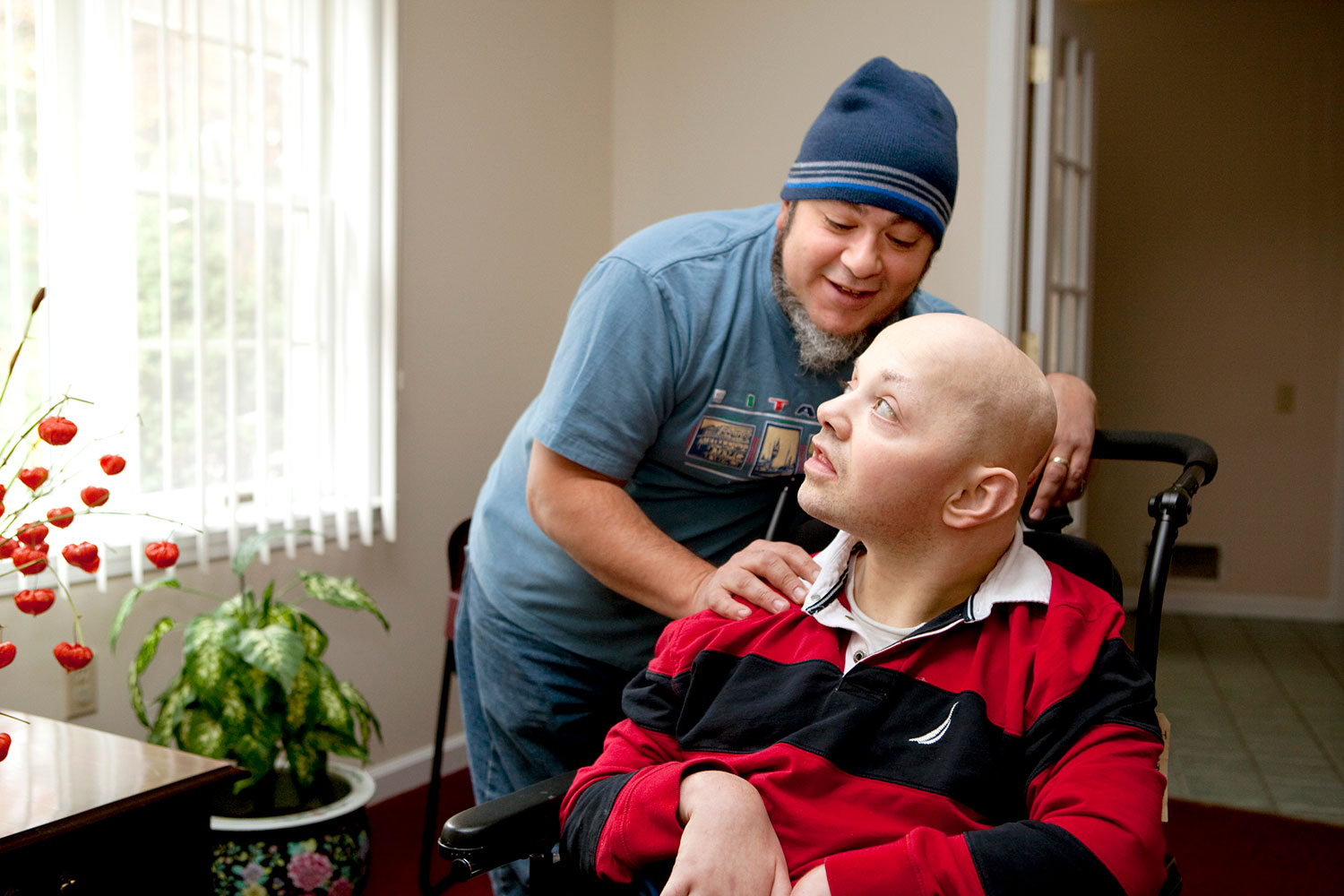 Man helps another man who is in a wheel chair.